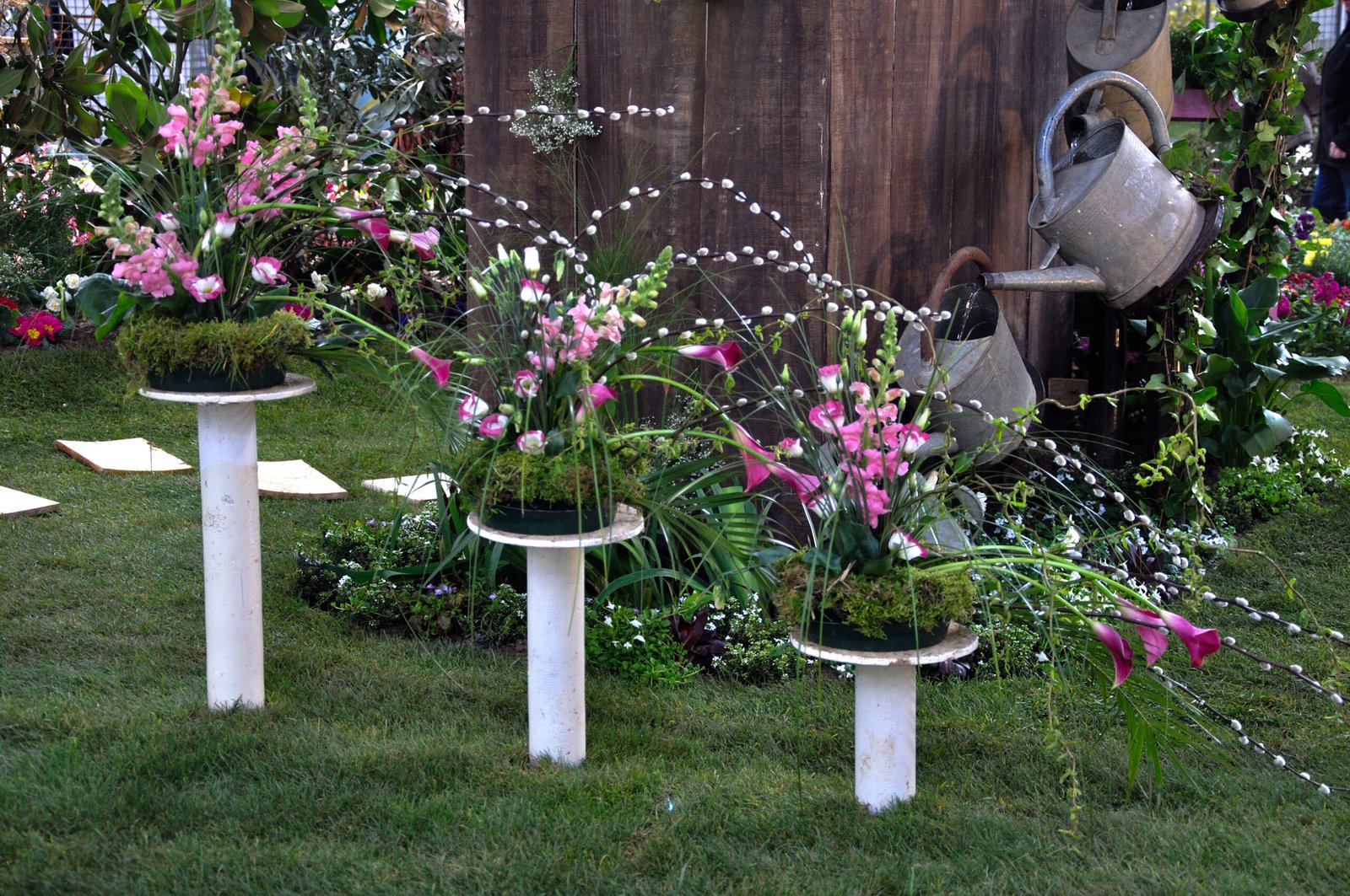 3 compositions florales à dominante rose posées sur 3 présentoirs blancs de hauteur croissante